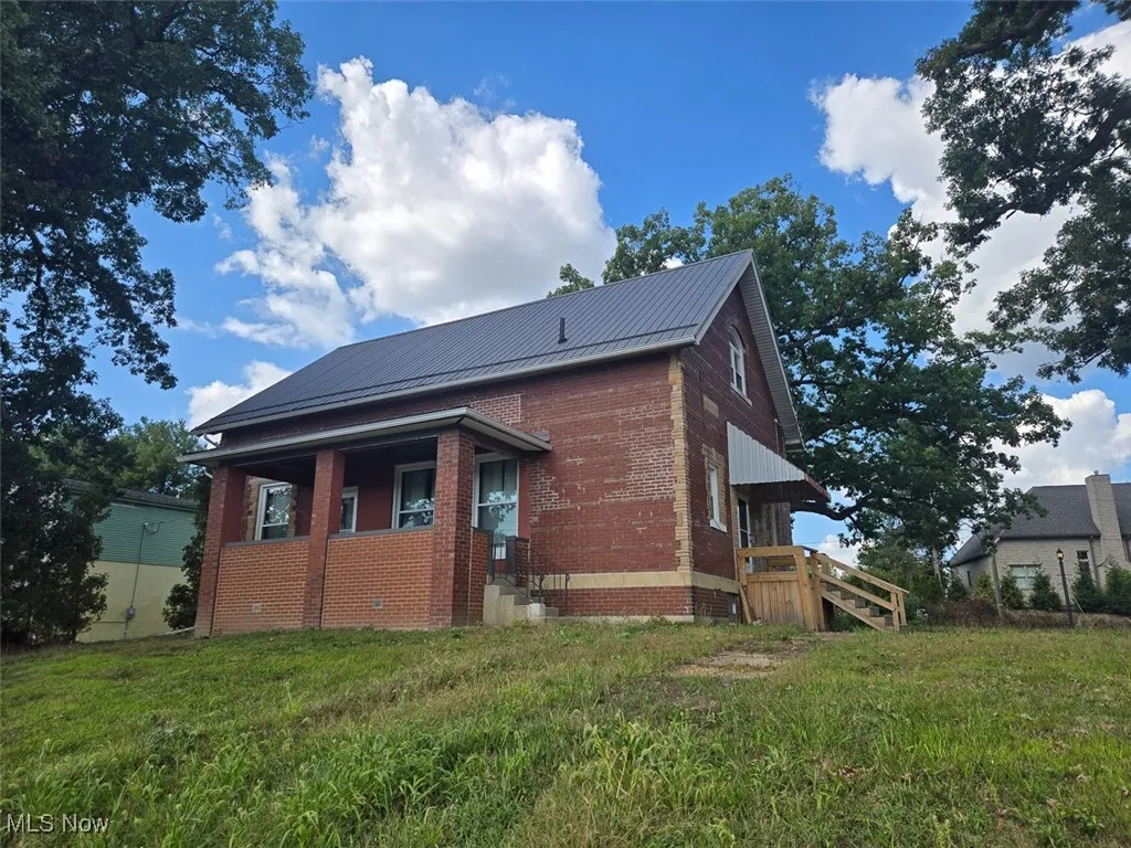 View of side of home featuring a yard, brick siding, and a metal roof