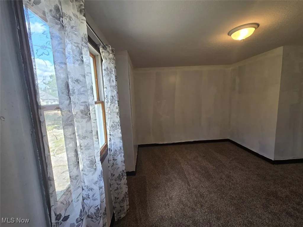 Unfurnished room featuring dark colored carpet, healthy amount of natural light, and a textured ceiling
