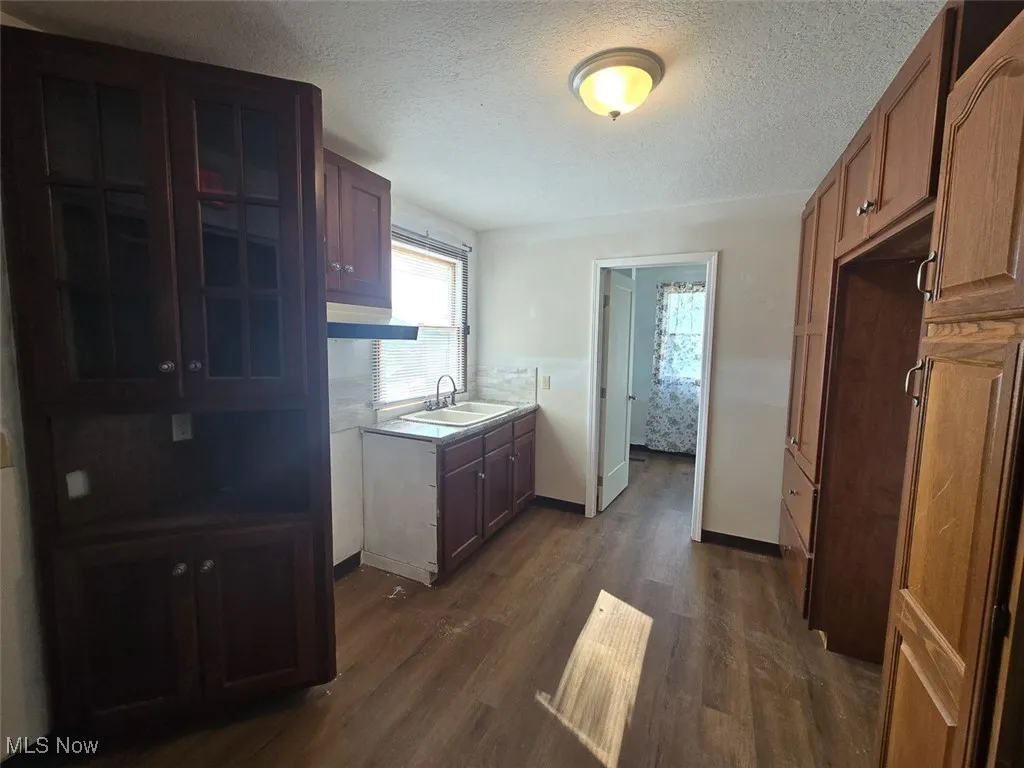 Kitchen featuring a textured ceiling, dark wood-style floors, custom exhaust hood, light countertops, and brown cabinets
