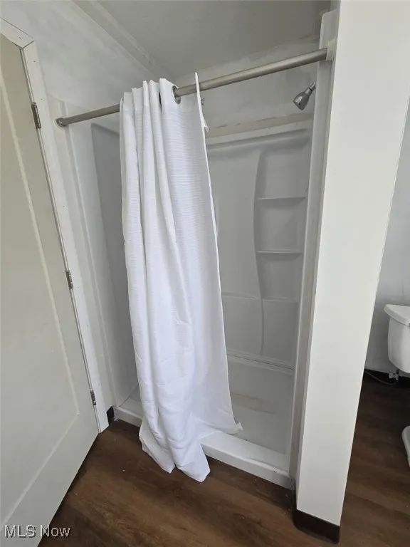 Full bath with a shower stall and dark wood-style flooring
