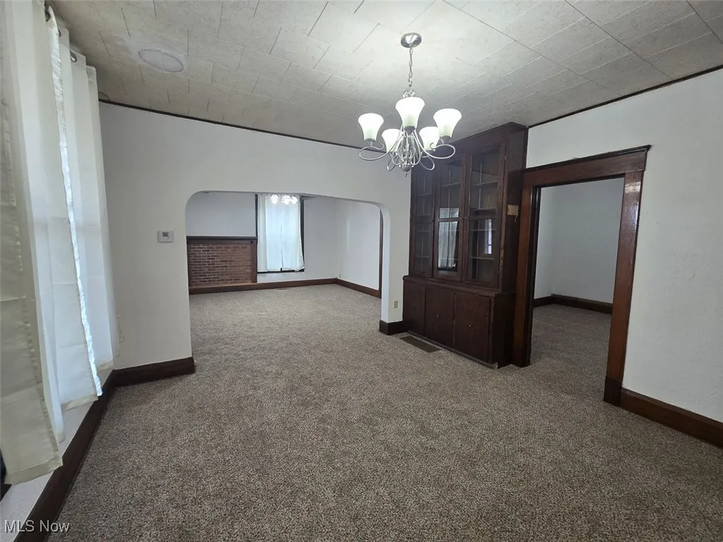 Carpeted spare room featuring arched walkways and a chandelier