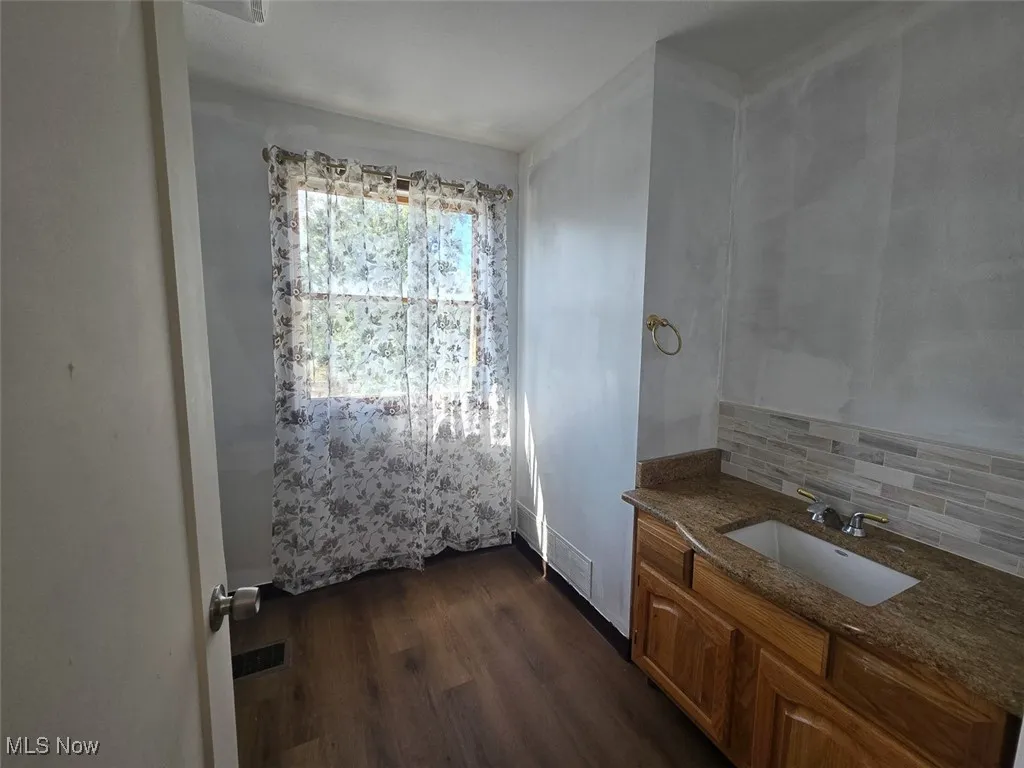 Bathroom featuring dark wood-style flooring, vanity, and decorative backsplash
