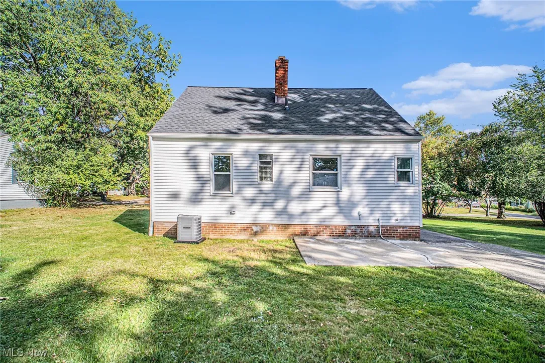 View of side of home featuring a yard, a patio, a chimney, and a shingled roof