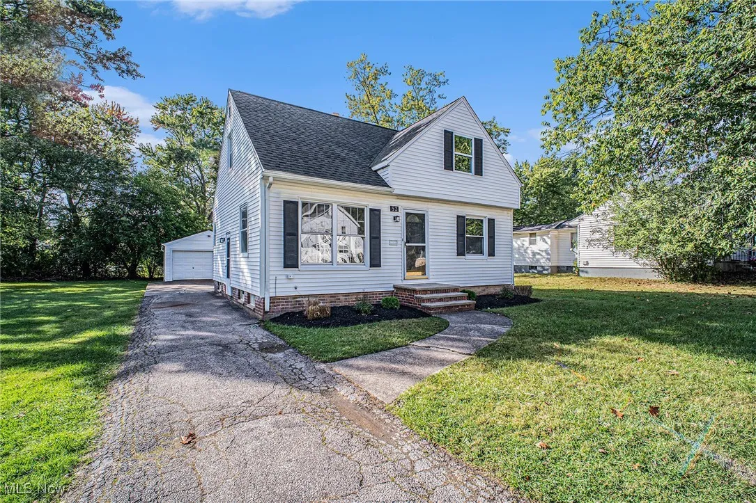 View of front facade featuring a front yard, a shingled roof, a garage, and an outbuilding