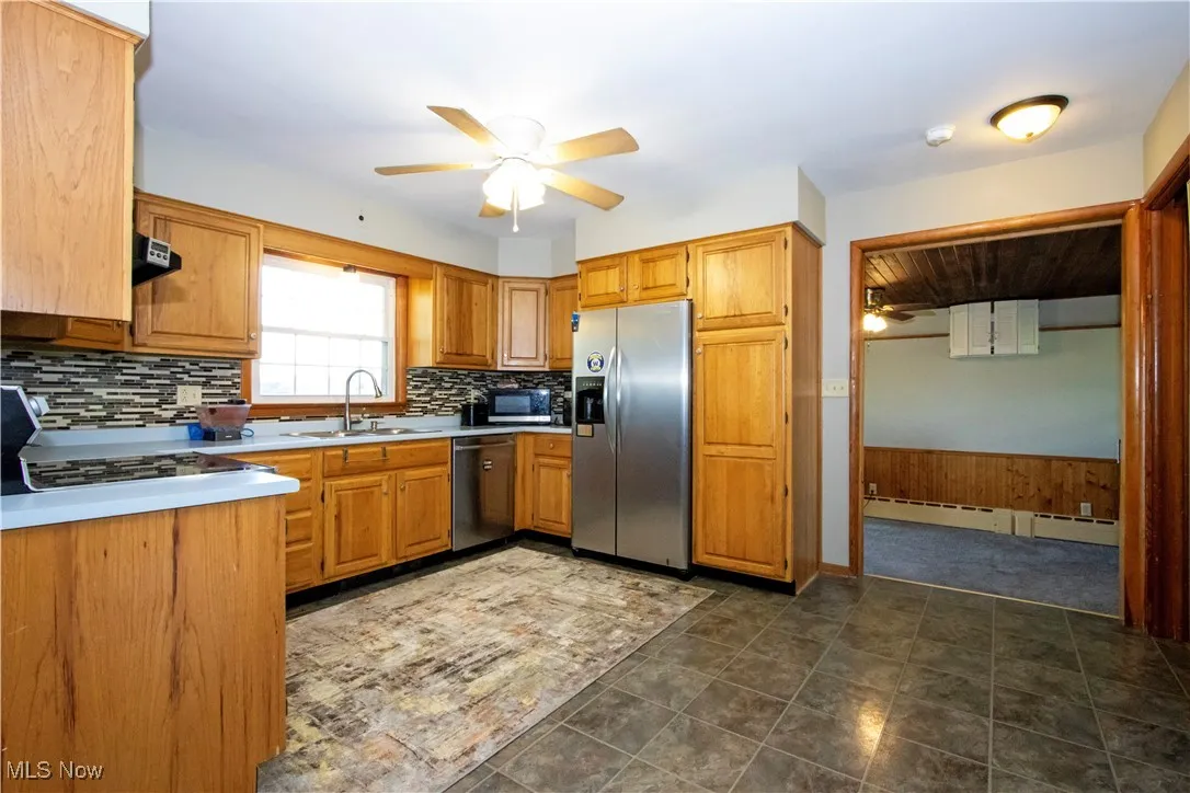 Kitchen featuring ceiling fan, appliances with stainless steel finishes, light countertops, wainscoting, and tasteful backsplash