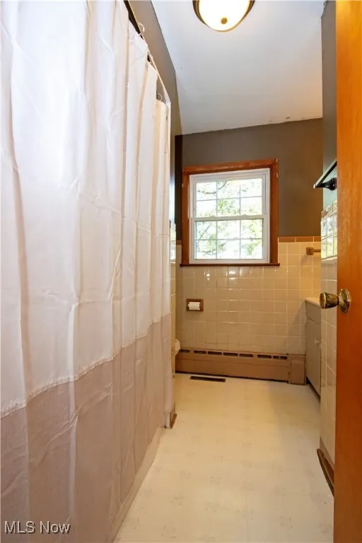 Bathroom featuring tile patterned floors, tile walls, vanity, a baseboard heating unit, and a wainscoted wall