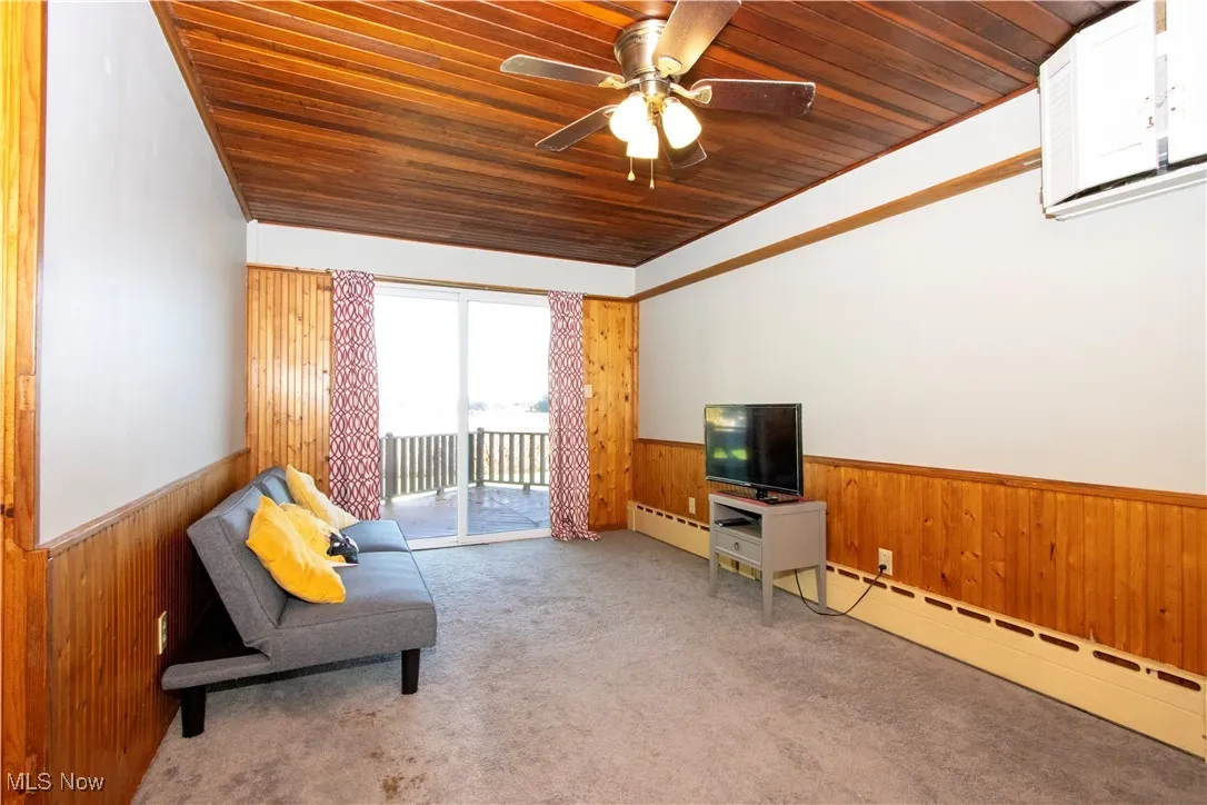 Living area featuring wooden walls, a wainscoted wall, wooden ceiling, baseboard heating, and carpet floors