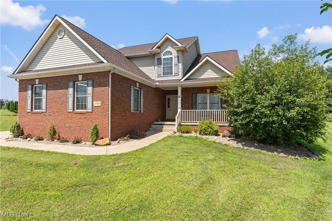 Traditional-style house featuring a porch, a front lawn, brick siding, and a shingled roof