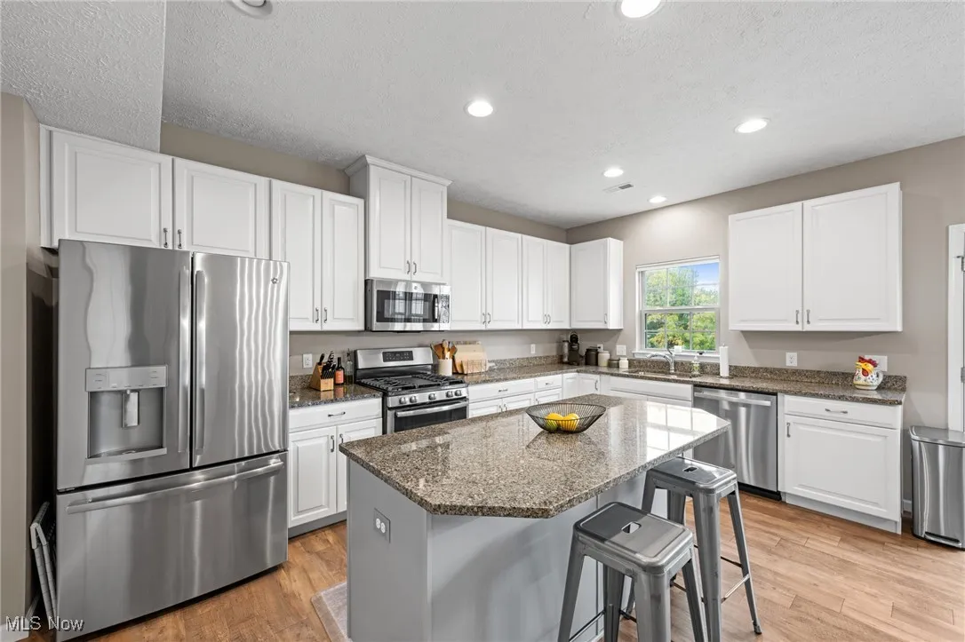 Kitchen with appliances with stainless steel finishes, wood-style floors, dark stone counters, recessed lighting, and a textured ceiling
