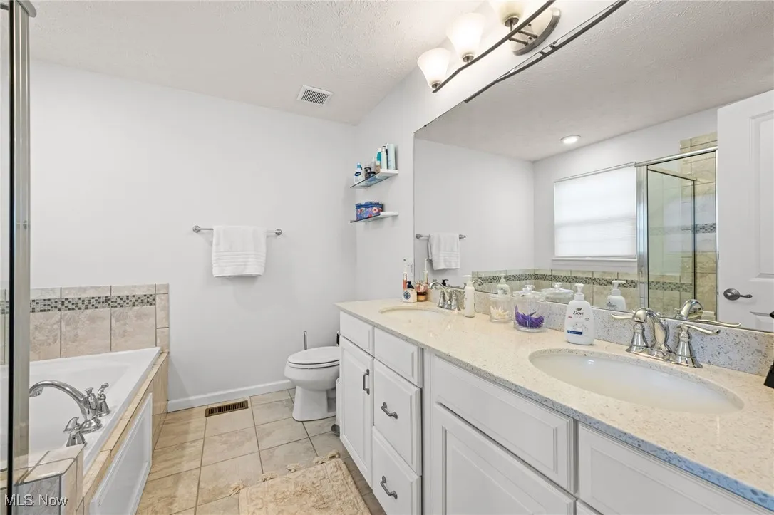 Owner's bathroom with double vanity, a bath, a textured ceiling, a stall shower, and light tile patterned floors