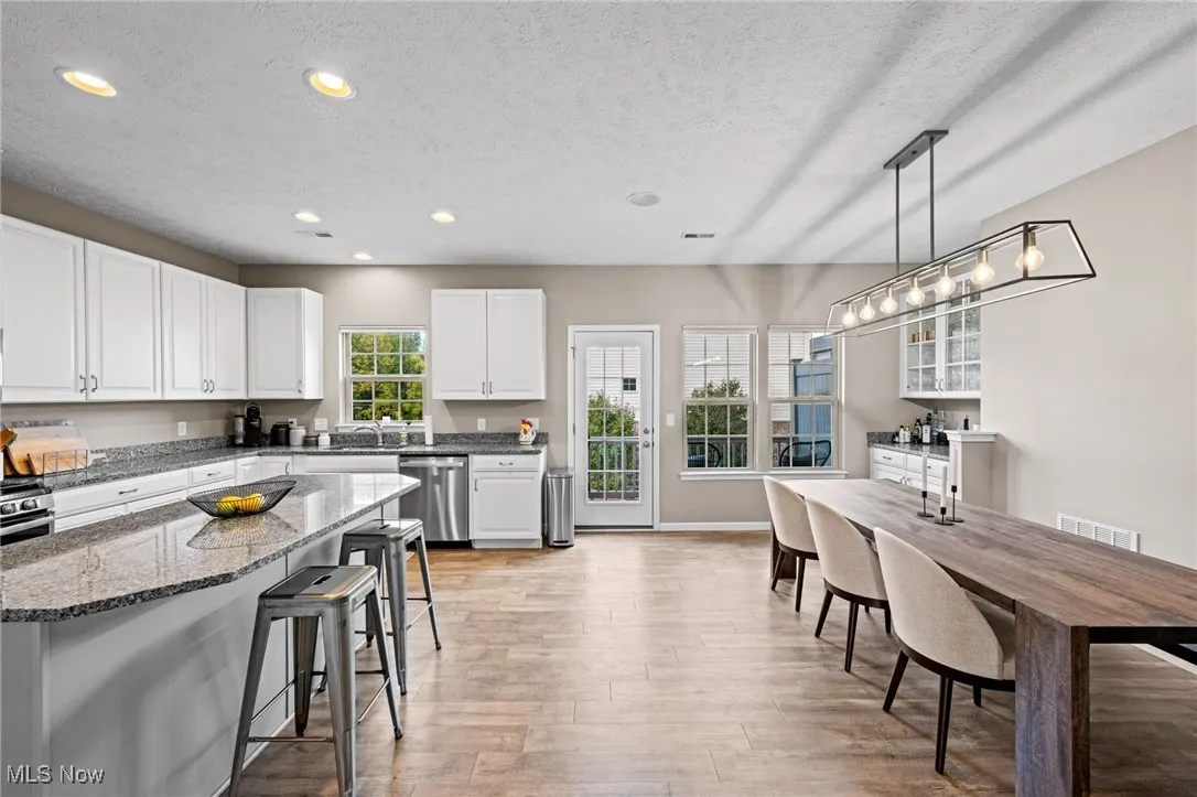 Kitchen with recessed lighting, a kitchen breakfast bar, white cabinets, a textured ceiling, and dark stone countertops