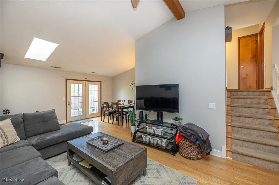 Living room with light wood-style flooring, a skylight, french doors, and stairs