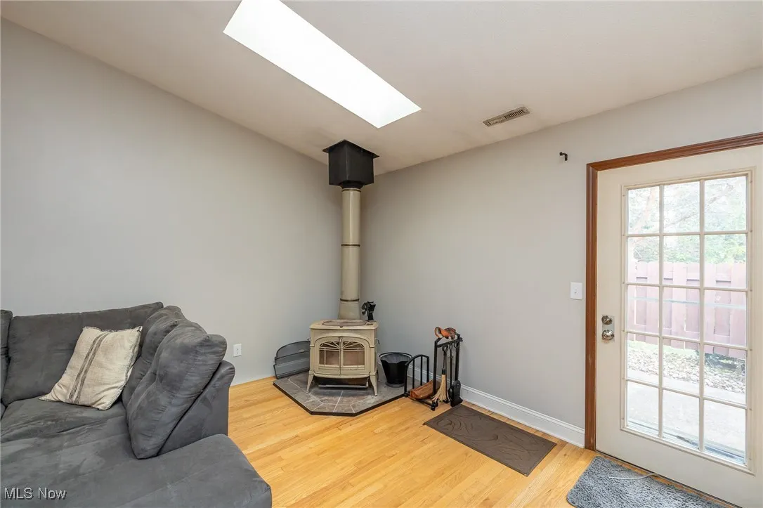 Living room featuring light wood-style floors, a skylight, and a wood stove