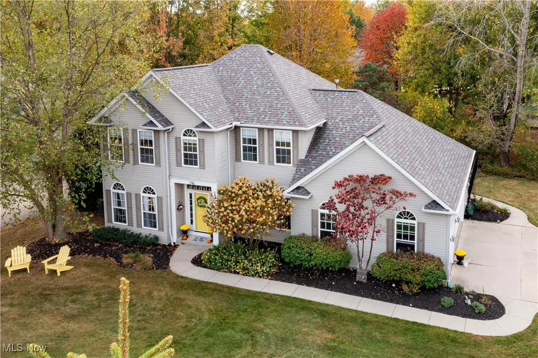 View of front facade with a front lawn, a shingled roof, and view of wooded area