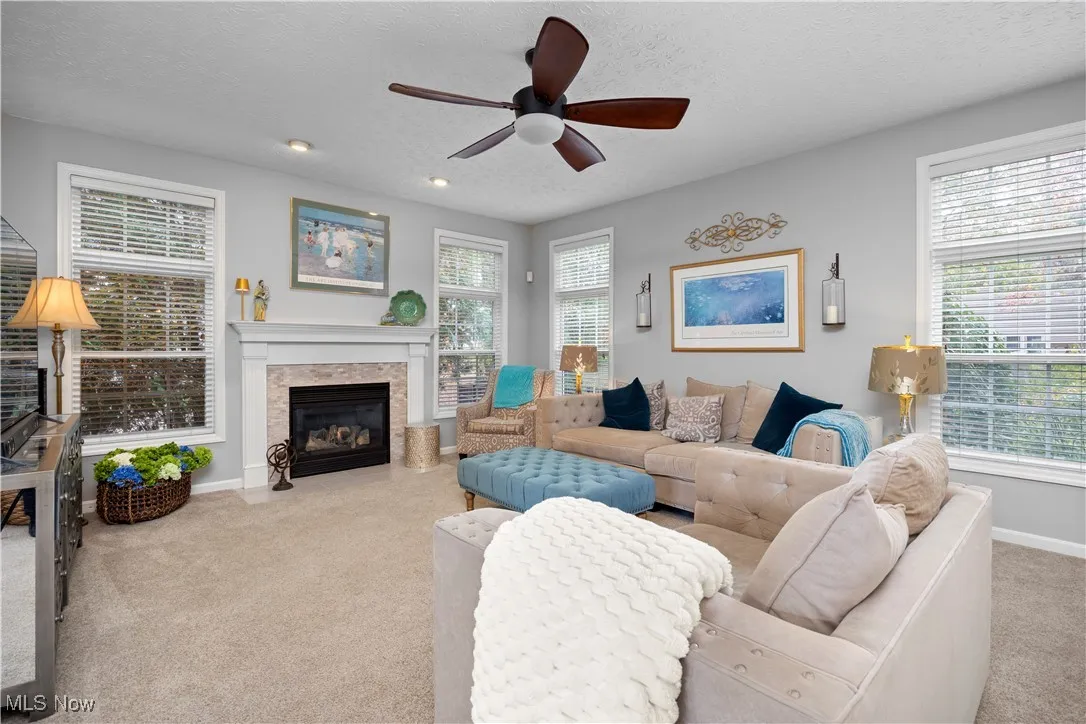 Family room featuring light carpet, a textured ceiling, ceiling fan, and a fireplace with flush hearth