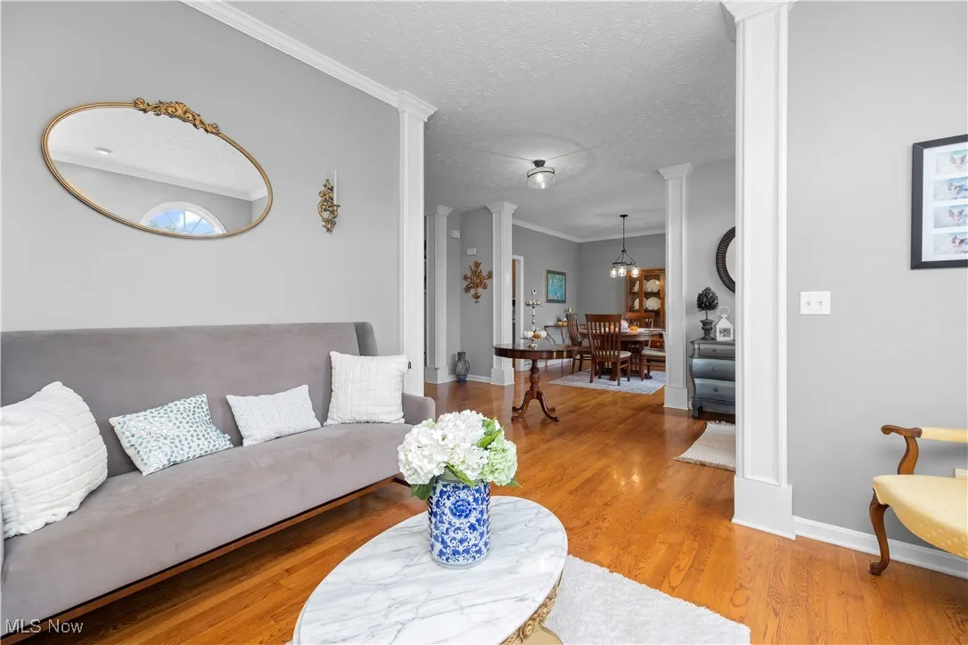 Living room with ornamental molding, a textured ceiling, wood finished floors, and ornate columns