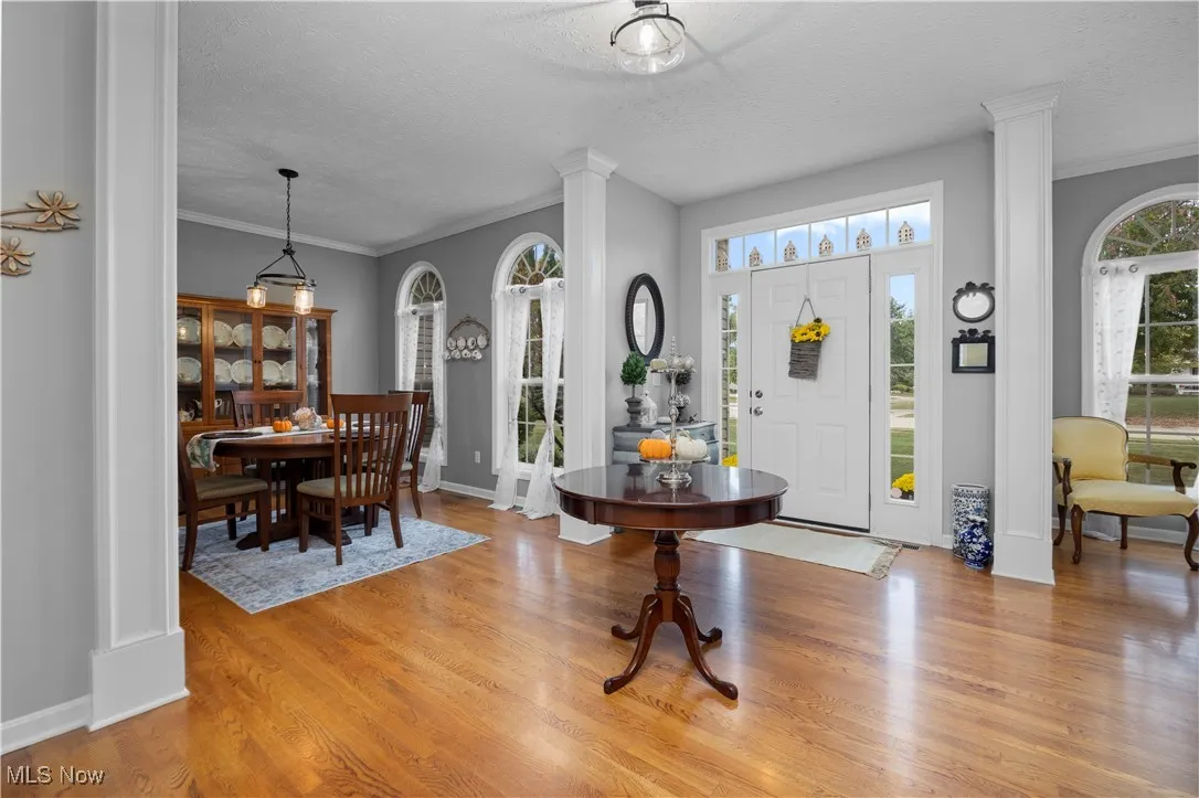 Entrance foyer with a textured ceiling, crown molding, decorative columns, and wood floors