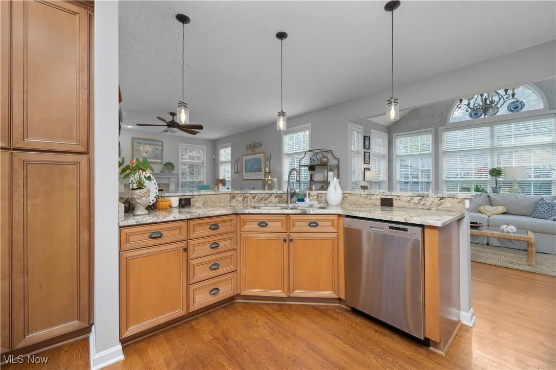 Kitchen featuring open floor plan, pendant lighting, dishwasher, maple cabinets, and light stone countertops