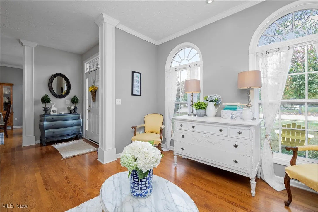 Sitting room with crown molding, wood finished floors, a textured ceiling, plenty of natural light, and decorative columns