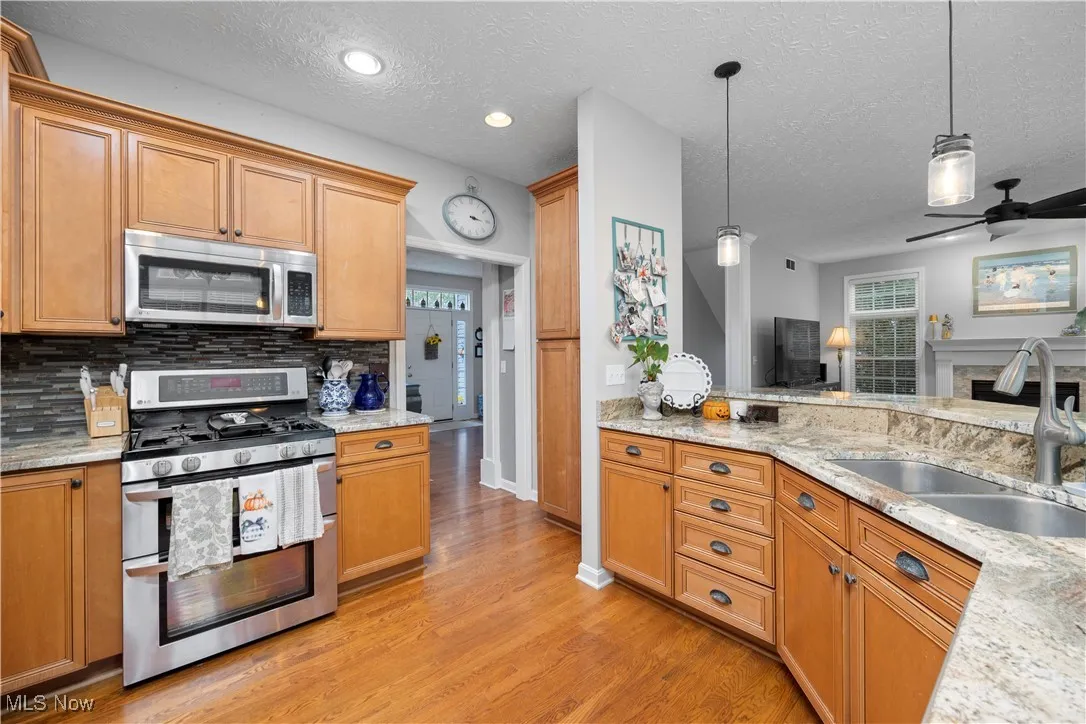 Kitchen featuring appliances with stainless steel finishes, light stone countertops, decorative light fixtures, a ceiling fan, and light wood finished floors