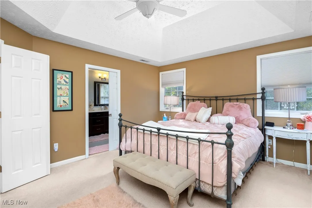 Bedroom featuring a textured ceiling, a raised ceiling, light carpet, a ceiling fan, and connected bathroom