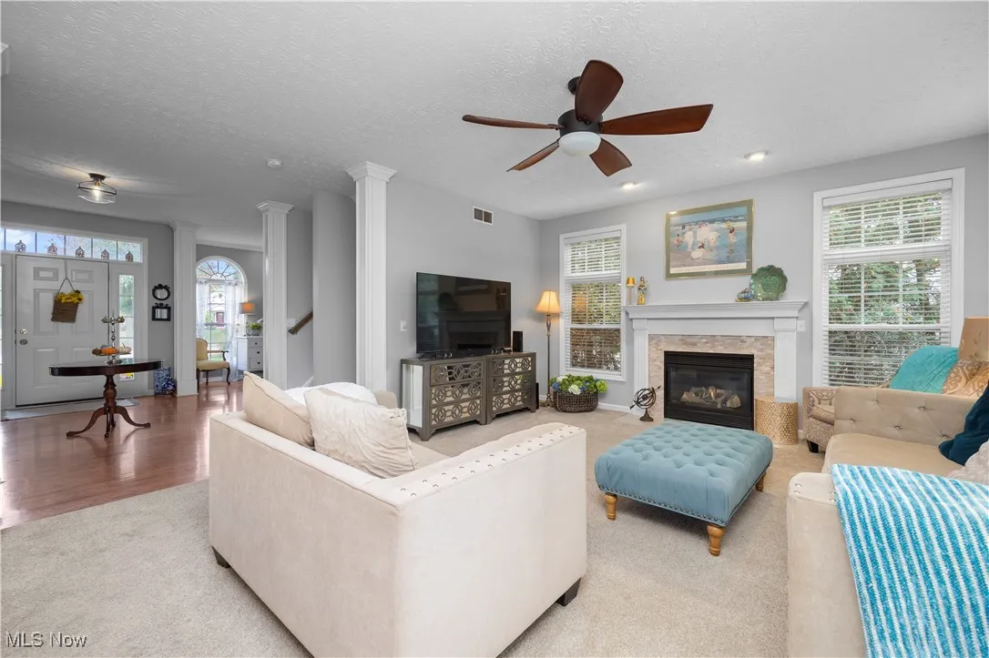 Carpeted living room with decorative columns, a textured ceiling, a ceiling fan, stairs, and a glass covered fireplace