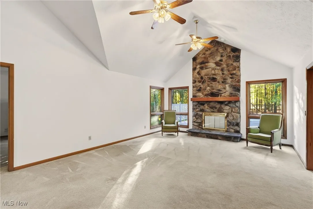 Unfurnished living room with high vaulted ceiling, a fireplace, light colored carpet, and ceiling fan