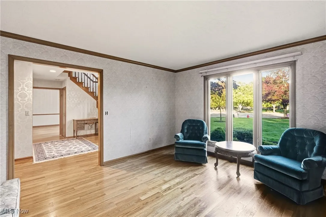 Living area with wallpapered walls, wood finished floors, ornamental molding, and stairs