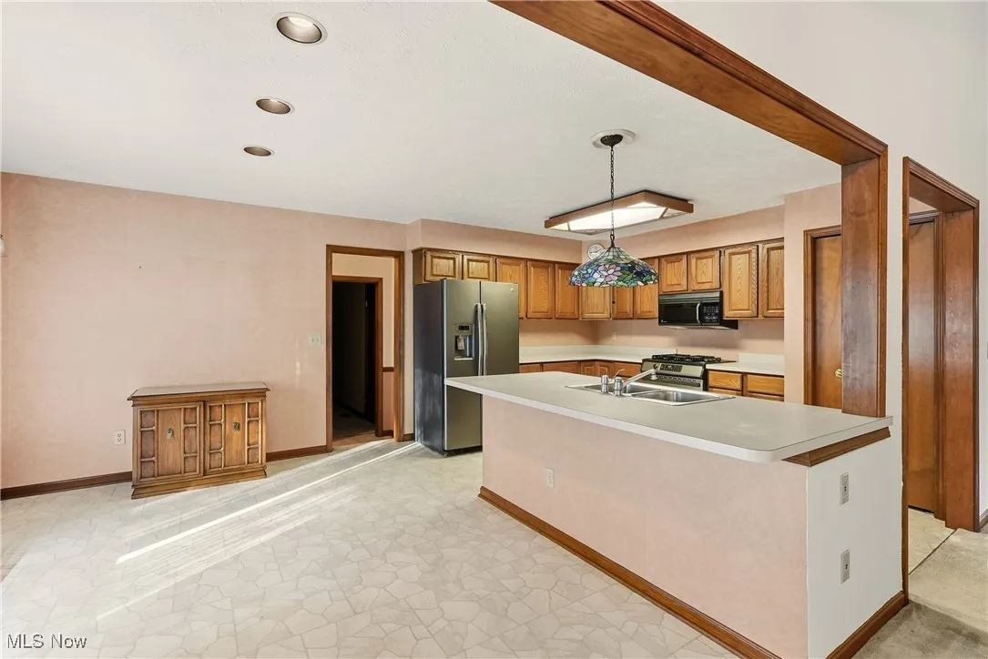 Kitchen featuring stainless steel appliances, light countertops, an island with sink, pendant lighting, and brown cabinetry