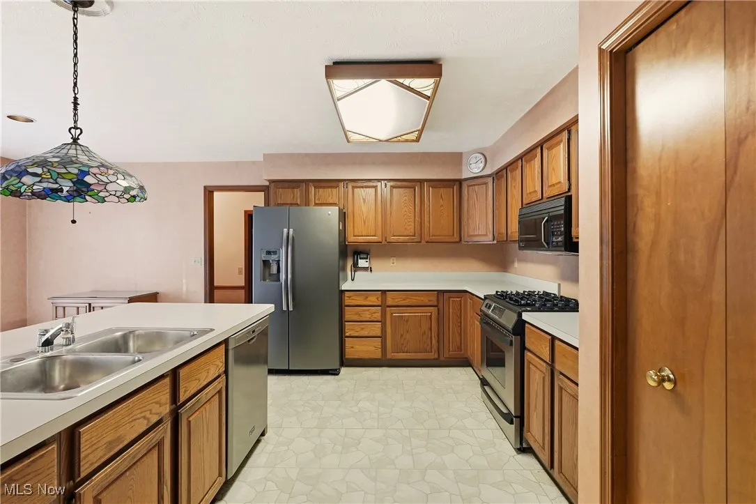 Kitchen with brown cabinets, stainless steel appliances, pendant lighting, and light countertops