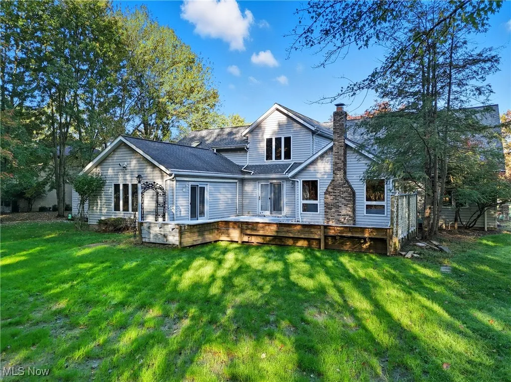 Rear view of property featuring a yard, a chimney, a deck, and roof with shingles