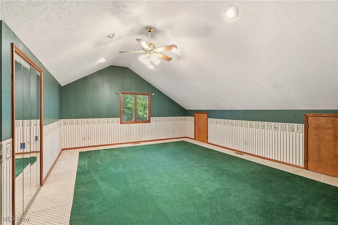 Bonus room with vaulted ceiling, carpet, a textured ceiling, ceiling fan, and wainscoting