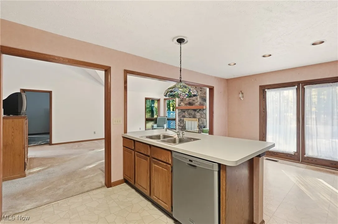 Kitchen featuring brown cabinets, stainless steel dishwasher, hanging light fixtures, light countertops, and plenty of natural light