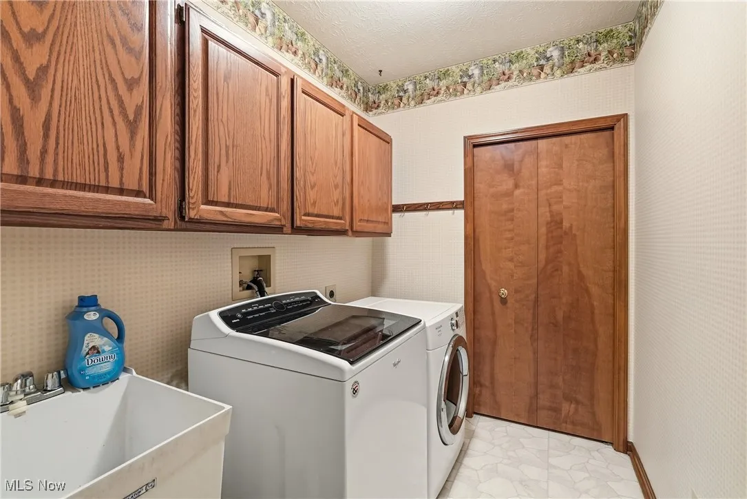 Laundry room featuring wallpapered walls, a textured ceiling, cabinet space, and washer and clothes dryer