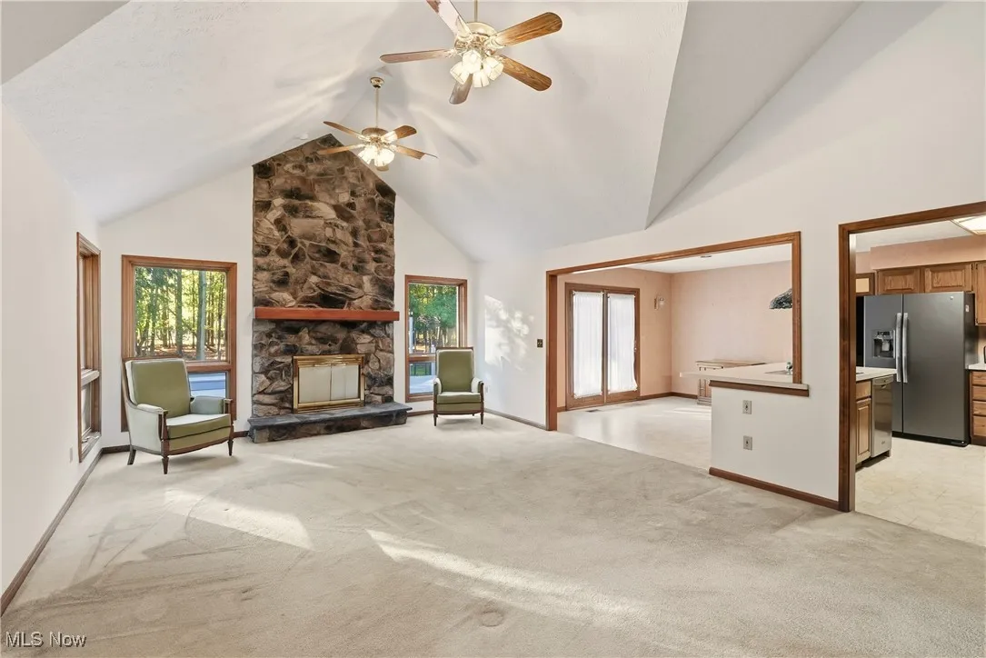 Unfurnished living room featuring high vaulted ceiling, light colored carpet, a stone fireplace, and ceiling fan