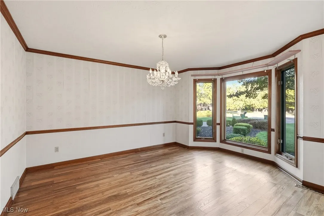 Unfurnished dining area featuring ornamental molding, wood finished floors, wallpapered walls, and a chandelier