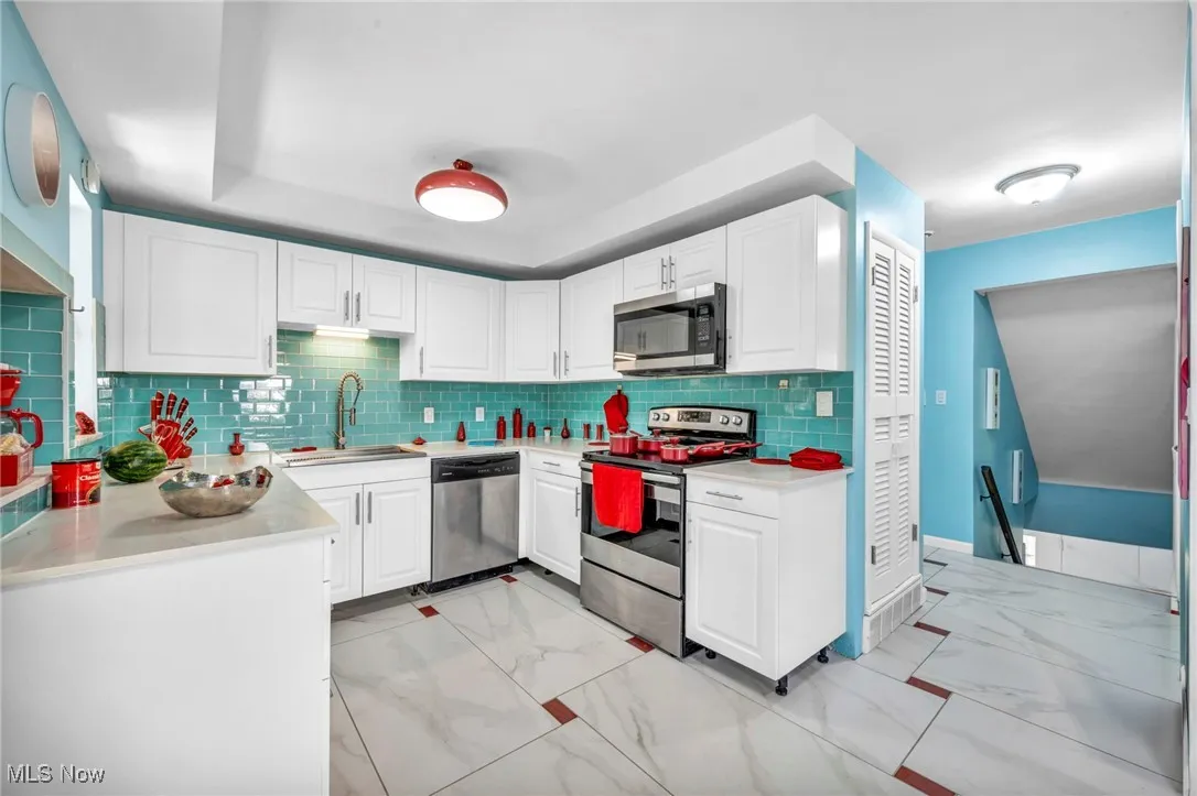 Kitchen featuring light marble finish floors, stainless steel appliances, white cabinetry, backsplash, and light stone counters