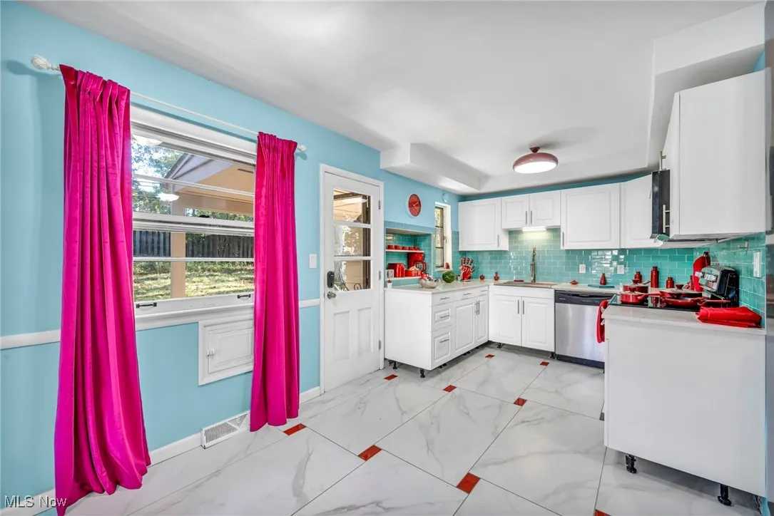 Kitchen featuring light countertops, decorative backsplash, light marble finish flooring, white cabinets, and dishwasher