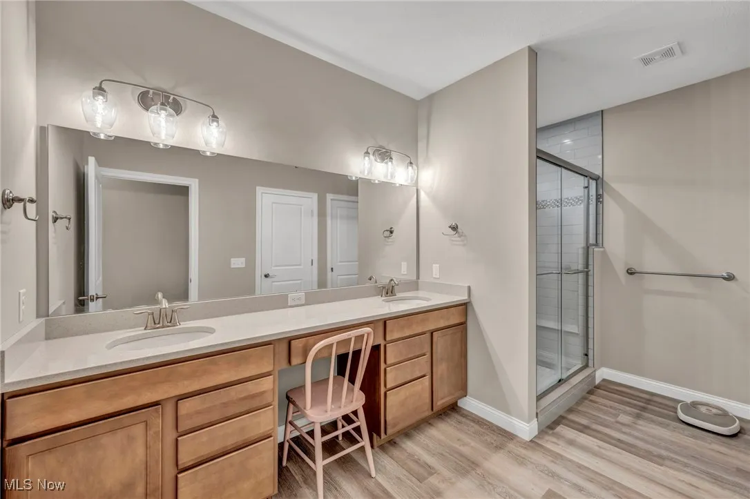 Bathroom with a shower stall, double vanity, and light wood finished floors