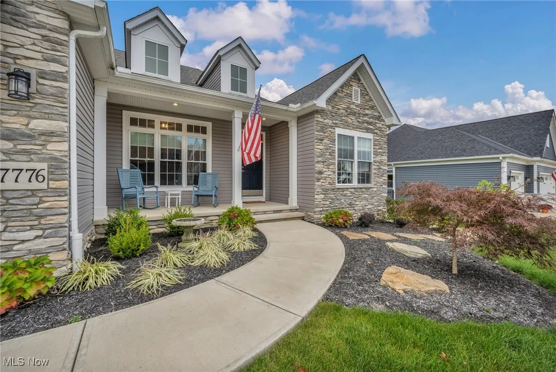 Entrance to property with stone siding, covered porch, and roof with shingles