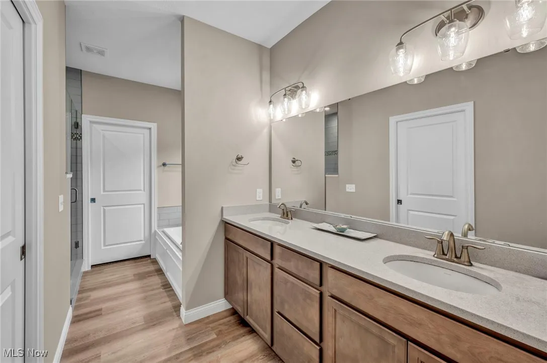 Bathroom with double vanity, light wood-style flooring, a garden tub, and a shower stall