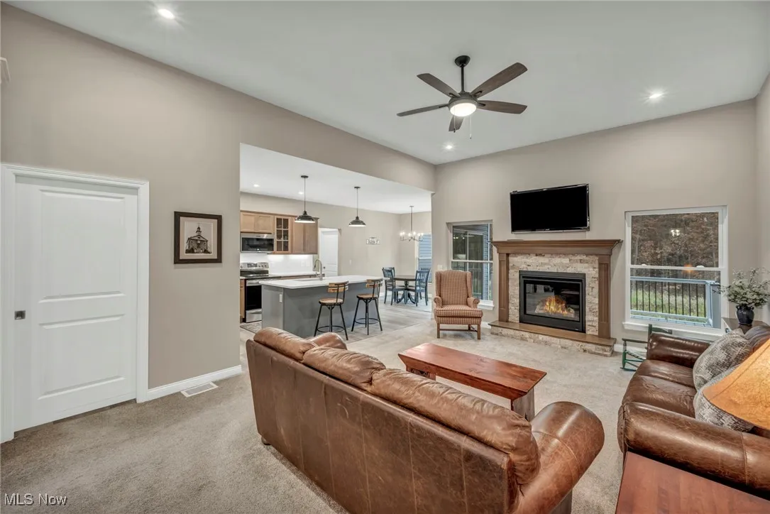 Living room with light carpet, a ceiling fan, a chandelier, a fireplace, and recessed lighting