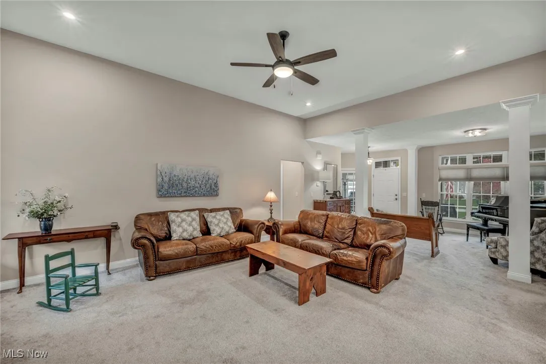 Carpeted living area featuring ceiling fan, decorative columns, and recessed lighting