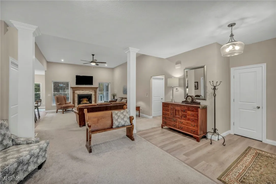 Living room with ornate columns, a ceiling fan, a warm lit fireplace, light carpet, and light wood-style flooring
