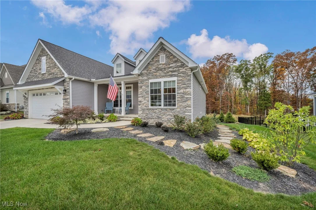 View of front of house featuring stone siding, a porch, a front yard, and a garage