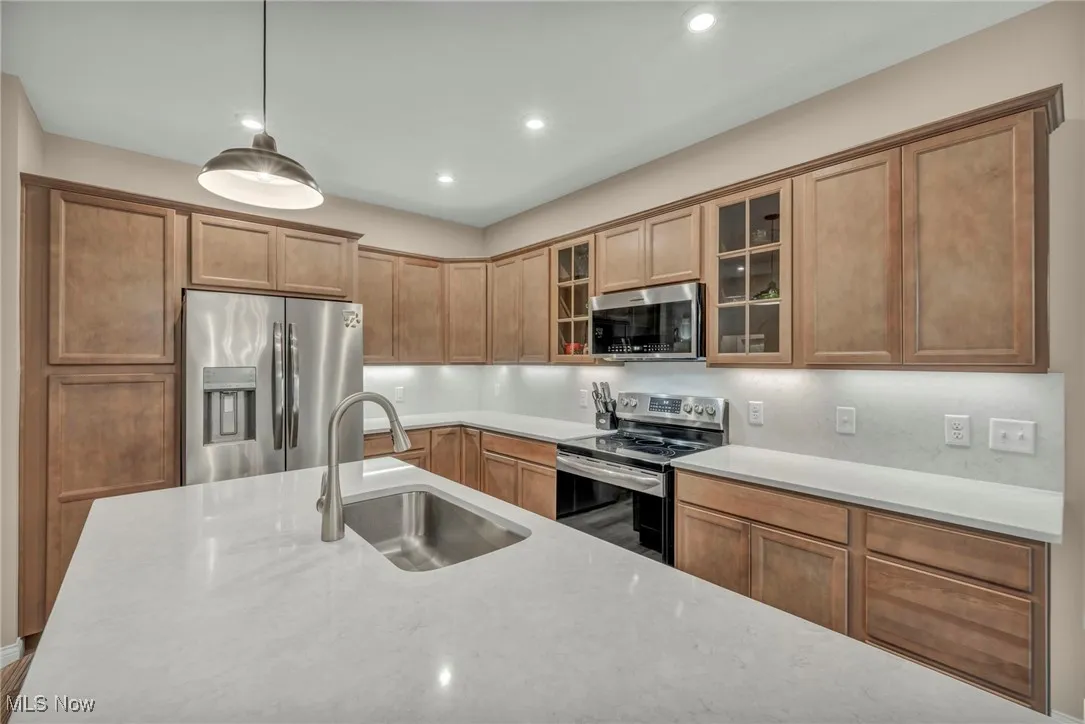 Kitchen with appliances with stainless steel finishes, glass insert cabinets, decorative light fixtures, light stone counters, and recessed lighting