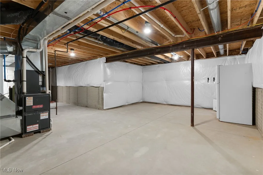Unfinished basement with freestanding refrigerator and heating unit