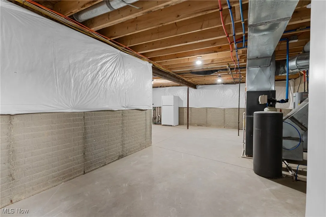Unfinished below grade area featuring freestanding refrigerator and a water softener system
