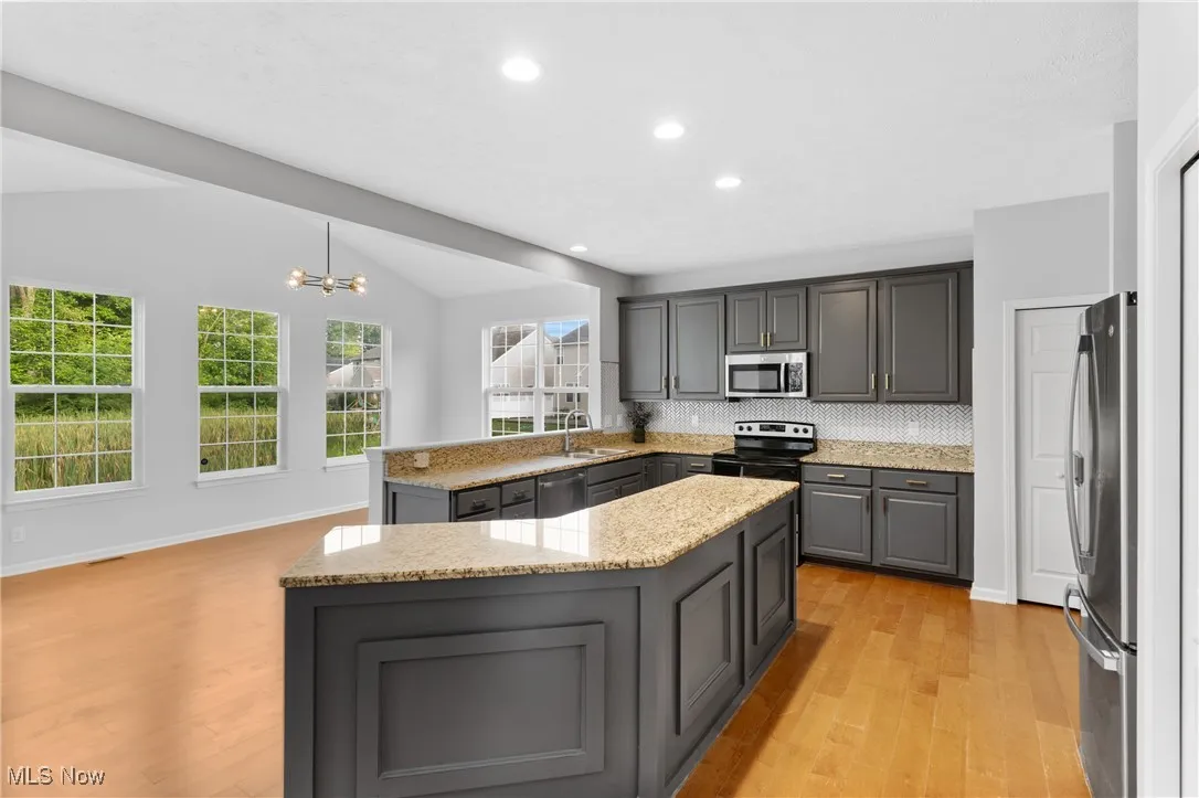 Kitchen featuring gray cabinetry, tasteful backsplash, a peninsula, light wood-style floors, and light stone counters