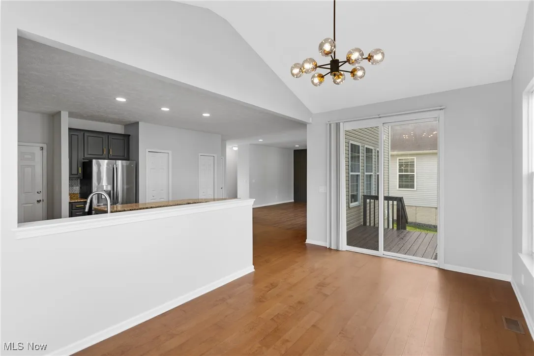 Unfurnished dining area with wood finished floors, a chandelier, recessed lighting, and high vaulted ceiling